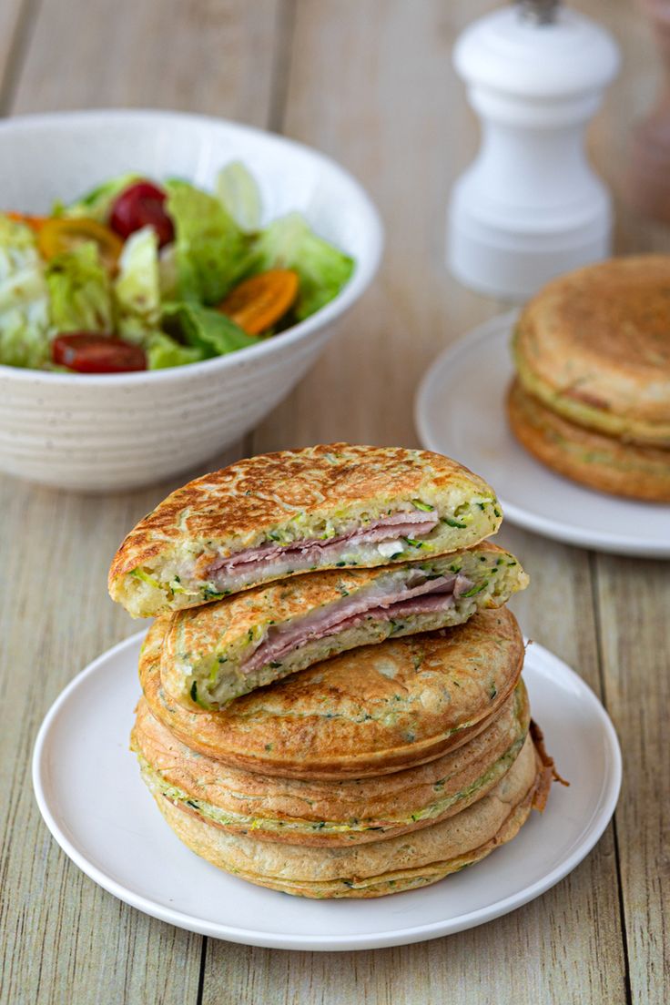 a stack of pancakes sitting on top of a white plate next to a bowl of salad