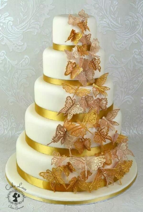 a three tiered wedding cake with gold butterflies on the top and bottom, sitting on a white plate