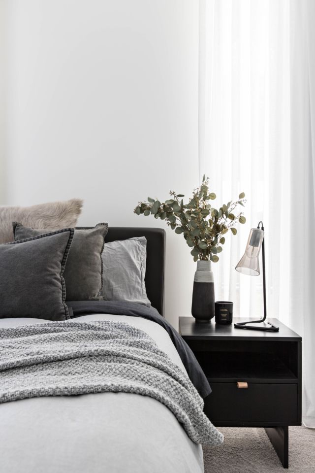 a bedroom with white walls and grey bedding is pictured in this image, there are two nightstands on either side of the bed