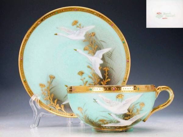 a tea cup and saucer with two birds painted on the side, sitting next to each other