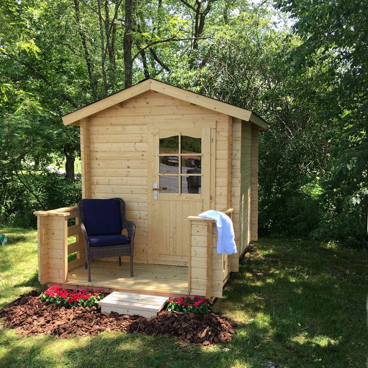 a small wooden shed with a blue chair in the yard next to flowers and trees