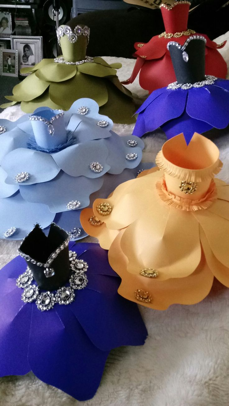 several different colors of paper flowers on a white blanket with diamond brooches in the center