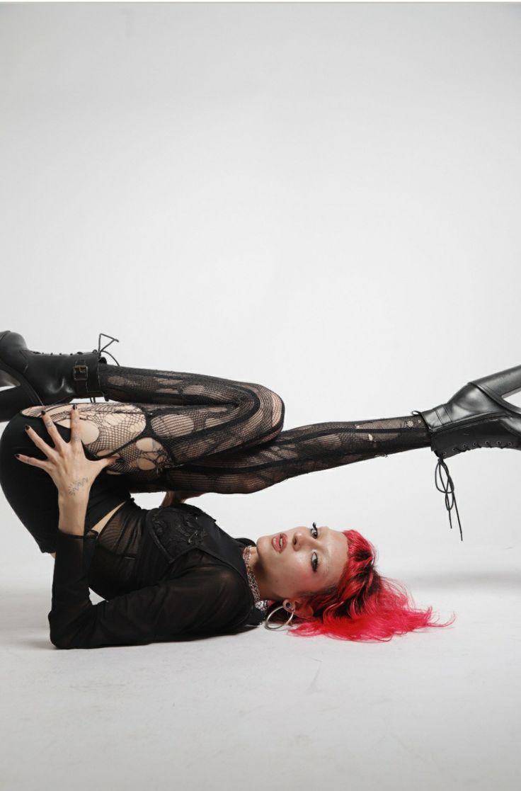 a woman with red hair is laying on the floor wearing black clothes and stockings, holding her leg up