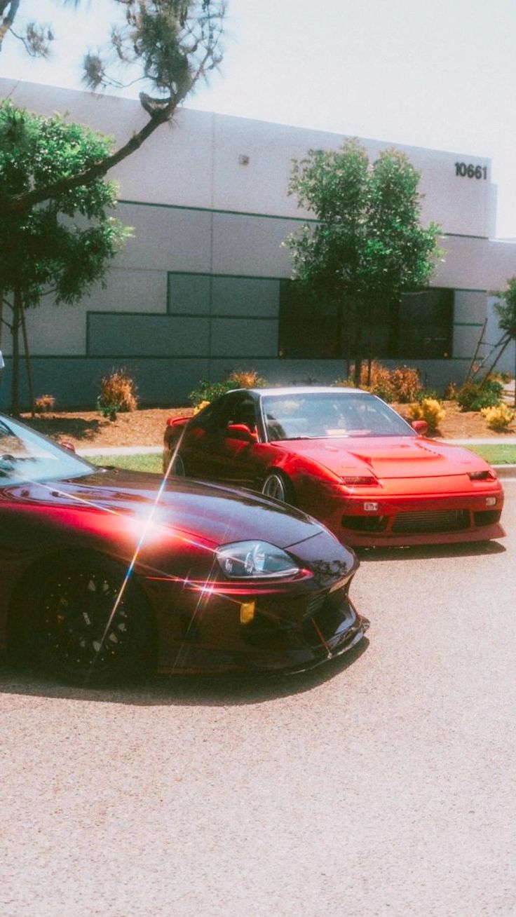 two red sports cars parked next to each other in front of a building with palm trees