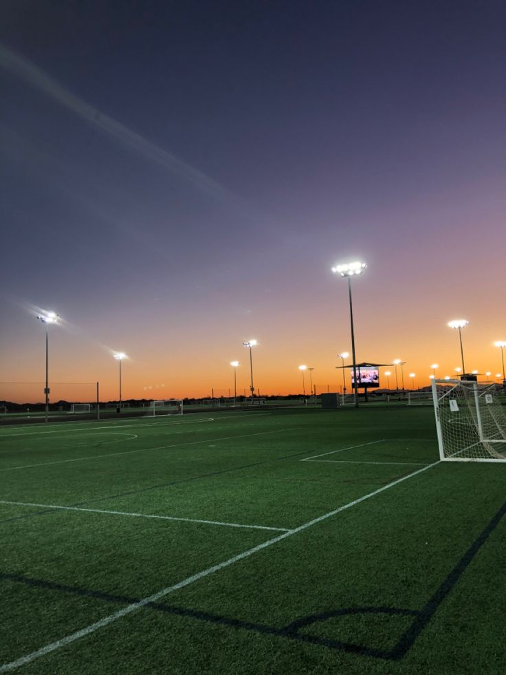 an empty soccer field at sunset with the lights on