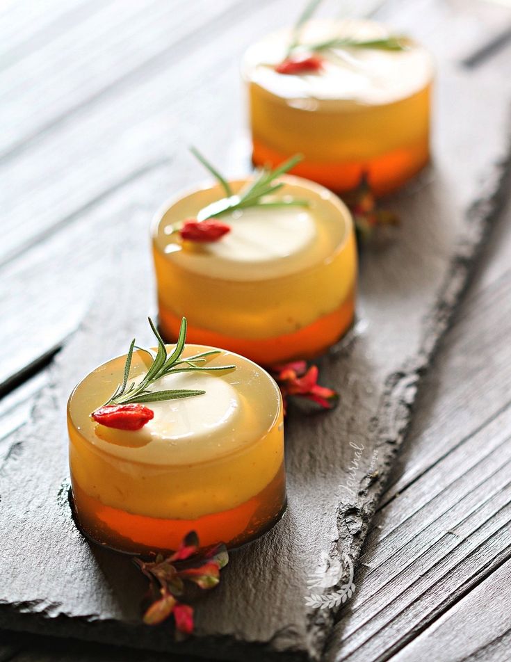 three small desserts are lined up on a slate board with rosemary garnishes