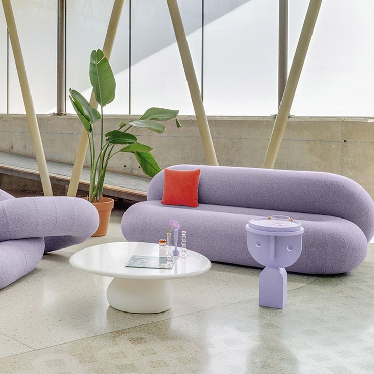 a living room filled with purple couches next to a white table and potted plant