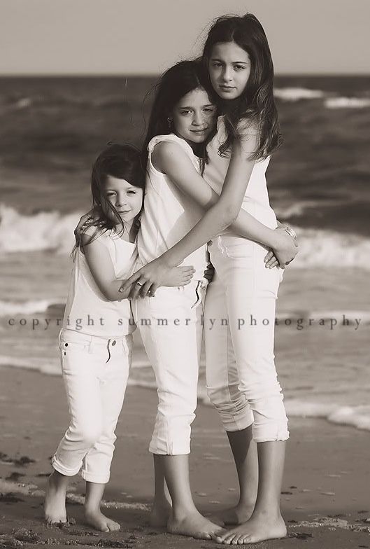 three girls standing on the beach with their arms around each other