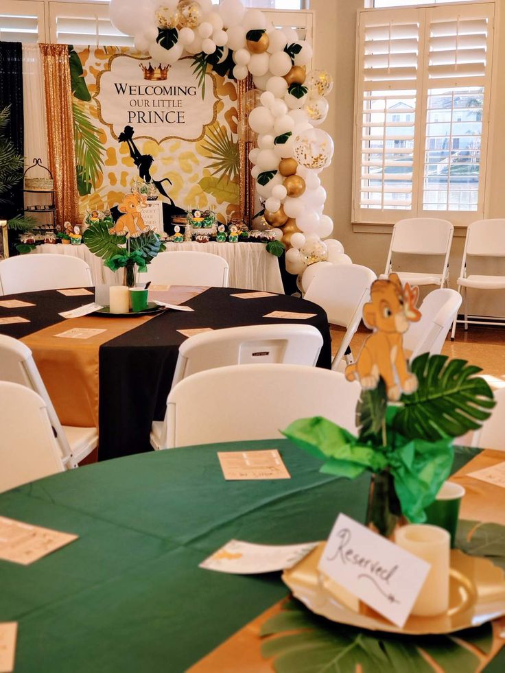 a room filled with tables and chairs covered in green table cloths, white balloons and jungle decorations