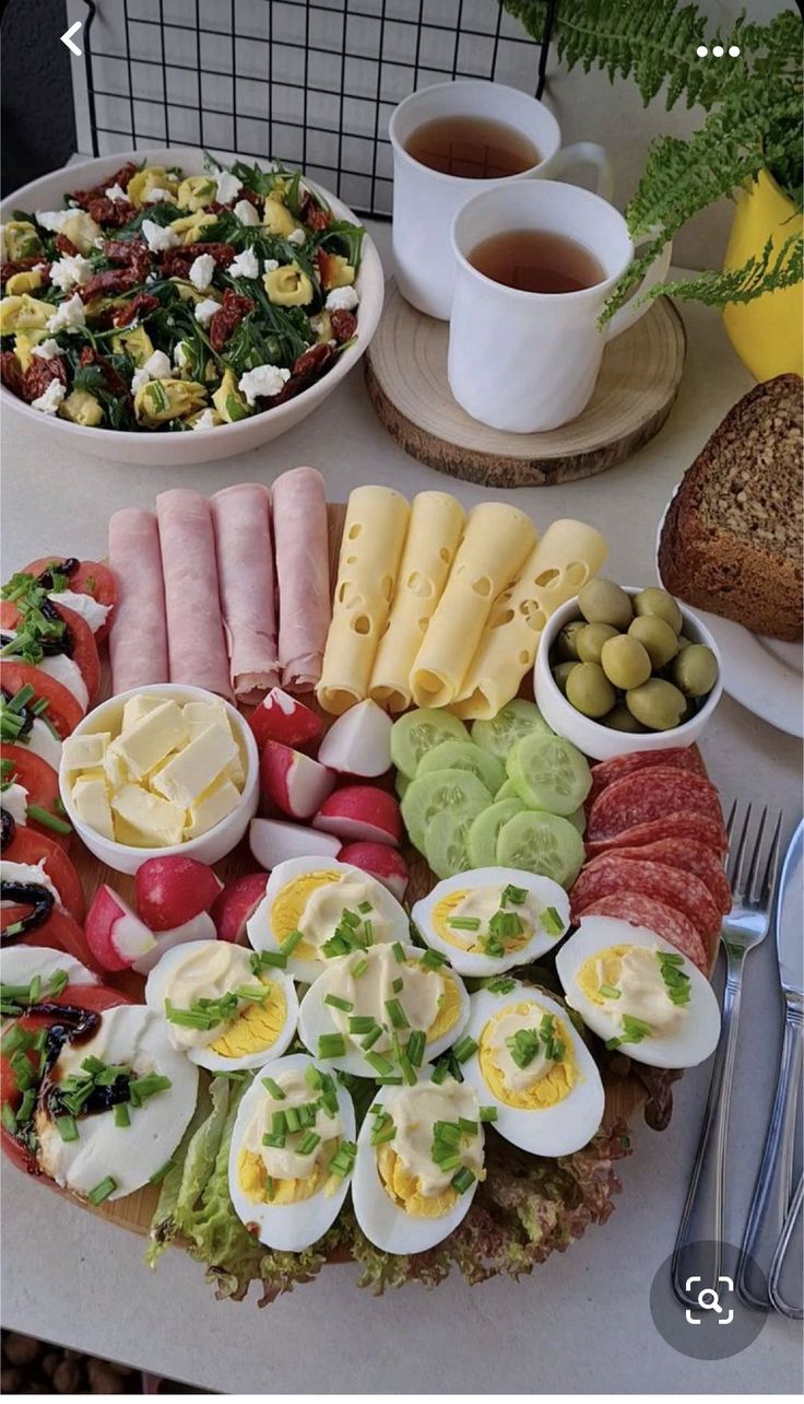 an assortment of food is displayed on a table with utensils and cups in front of it