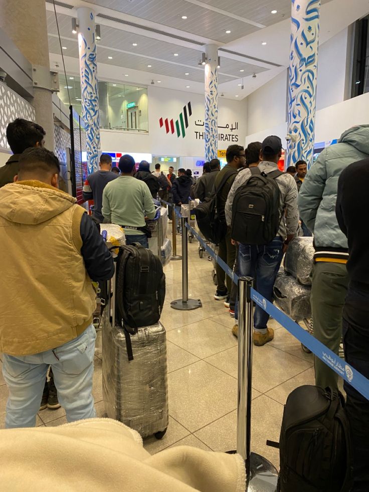 people waiting in line at an airport for their luggage