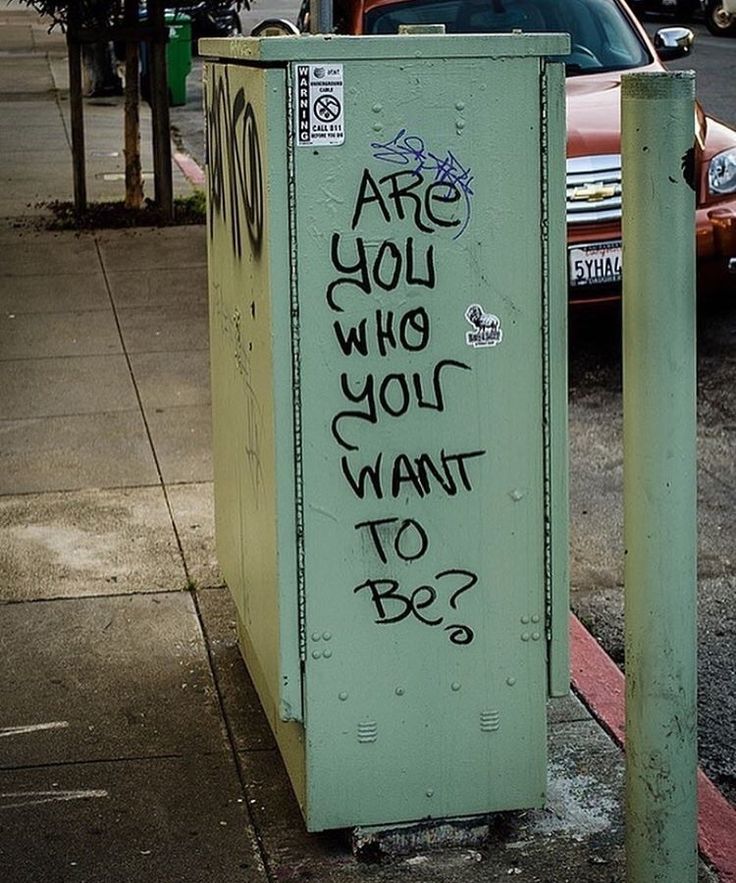 graffiti on the side of a parking meter in front of a street with parked cars