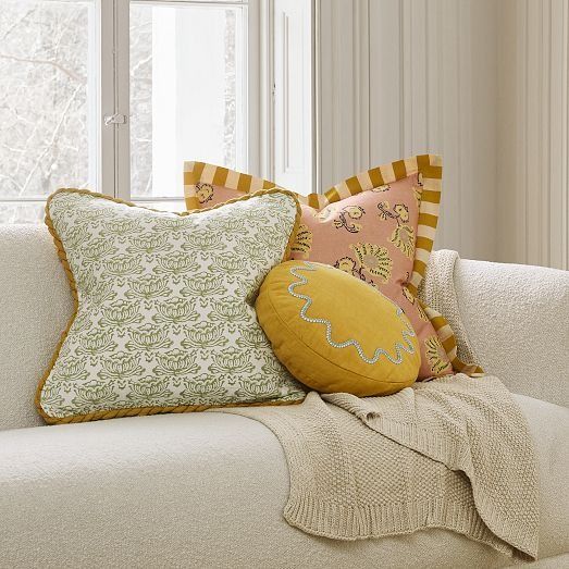 a white couch with pillows on top of it and a window in the back ground