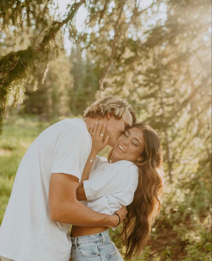 a young man and woman embracing each other in front of some trees with the sun shining on them