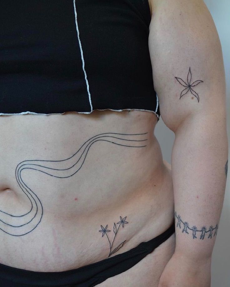 a woman's stomach with tattoos on the side and an outline of a flower