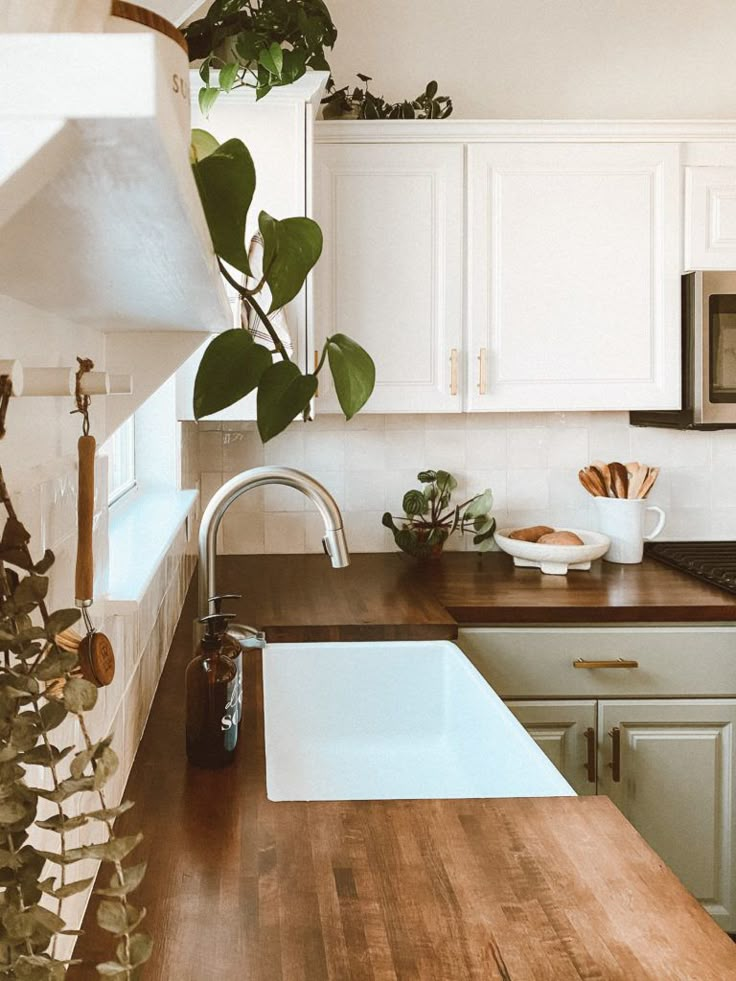 a kitchen with white cabinets and wooden counter tops, plants in the window sill