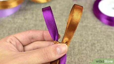 a hand holding a purple ribbon in front of some other ribbons on the floor and table