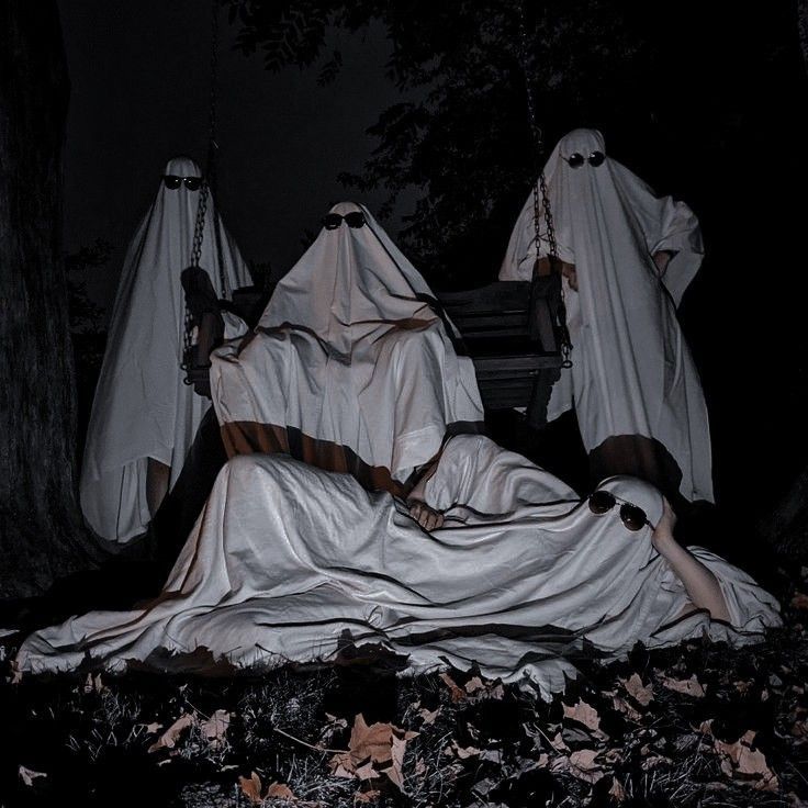 three ghostly people sitting on a bench in the woods with their heads covered by white cloths