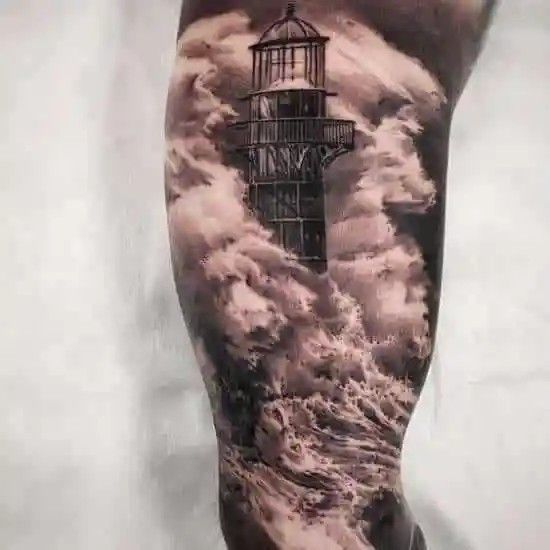 a man's leg with a lighthouse tattoo on it and clouds in the sky