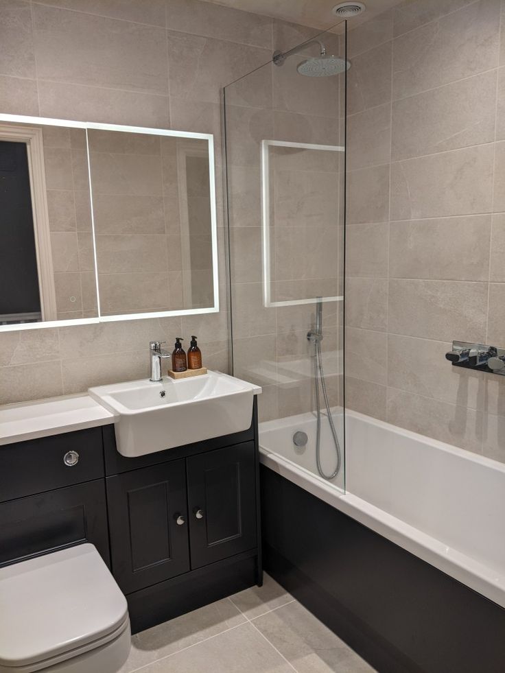 a white toilet sitting next to a bath tub under a bathroom mirror above a sink