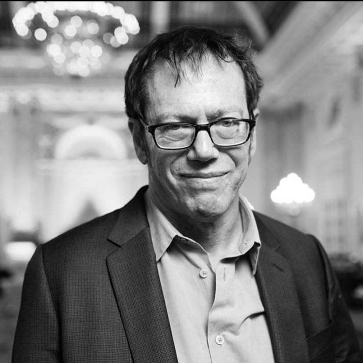 a black and white photo of a man with glasses smiling at the camera in a building