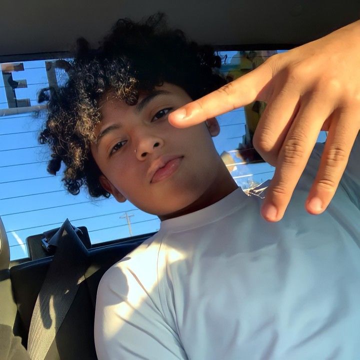 a young boy sitting in the back seat of a car with his hand on the steering wheel