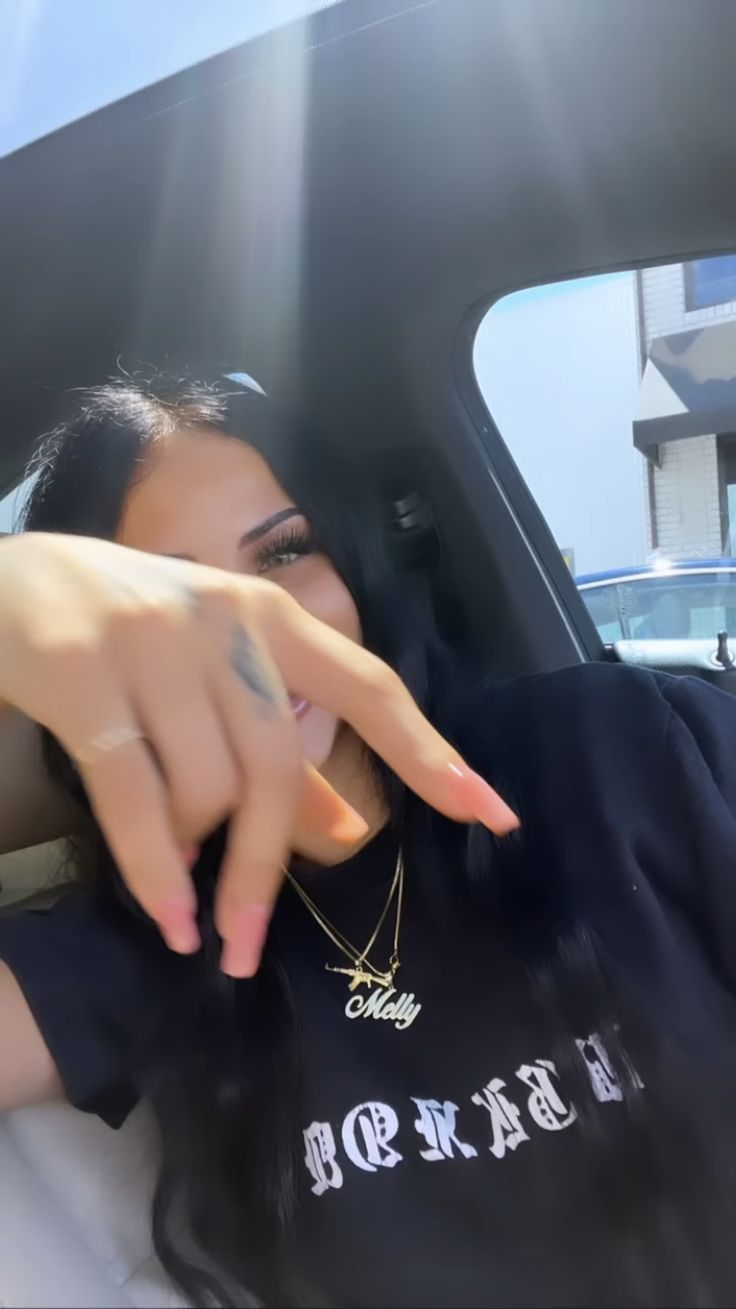 a woman pointing at the camera with her hand in front of her face and wearing a black t - shirt