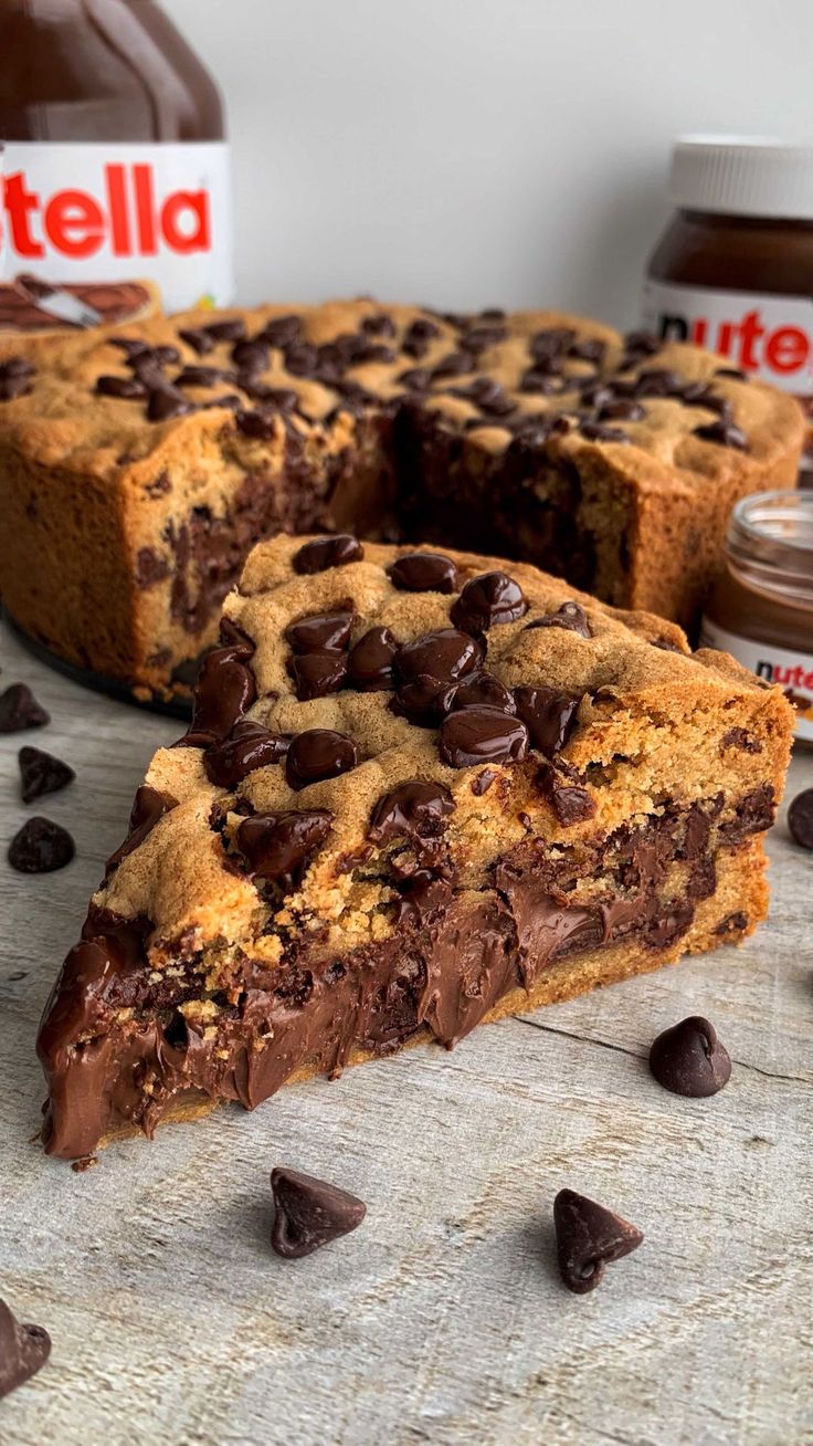 a chocolate chip cookie cake sitting on top of a table next to a jar of nutella