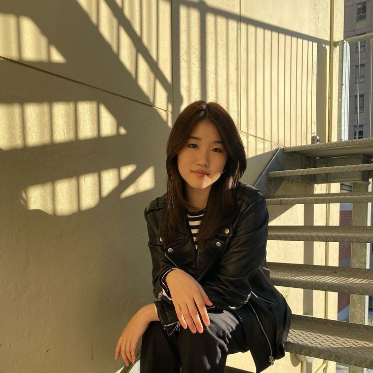 a young woman sitting on the steps in front of a building with her hand on her chin