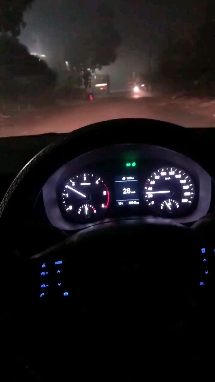 the dashboard of a car at night with lights on and fog in the air behind it