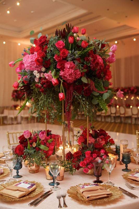 a tall vase filled with red and pink flowers on top of a white table cloth