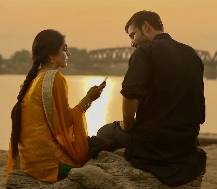 a man and woman sitting next to each other looking at something on their cell phone