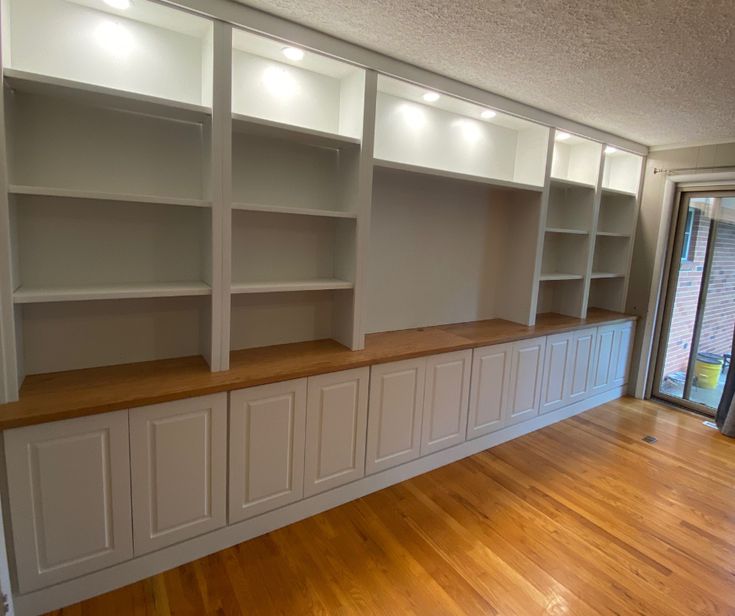 an empty room with white bookcases and wood floors