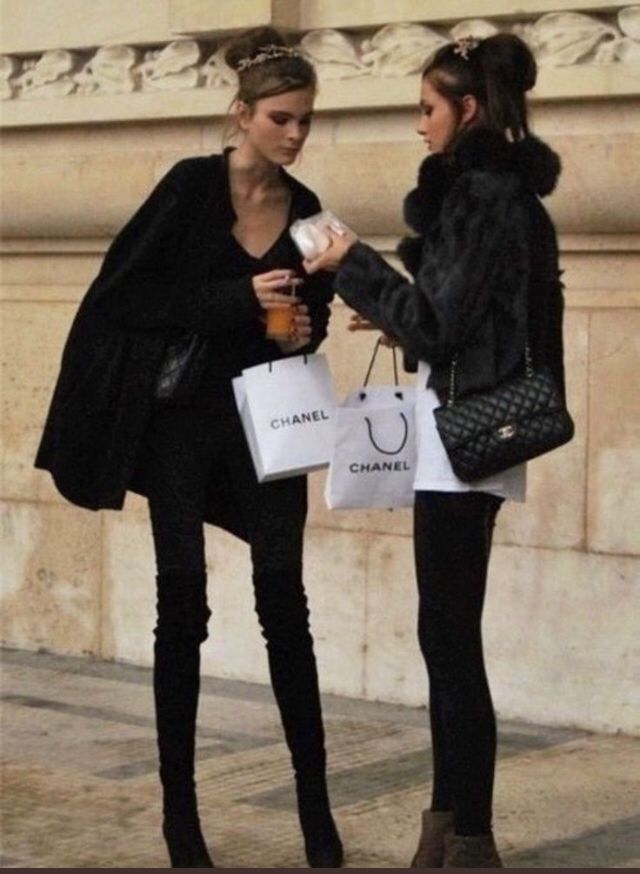 two young women standing next to each other holding shopping bags and talking on the street