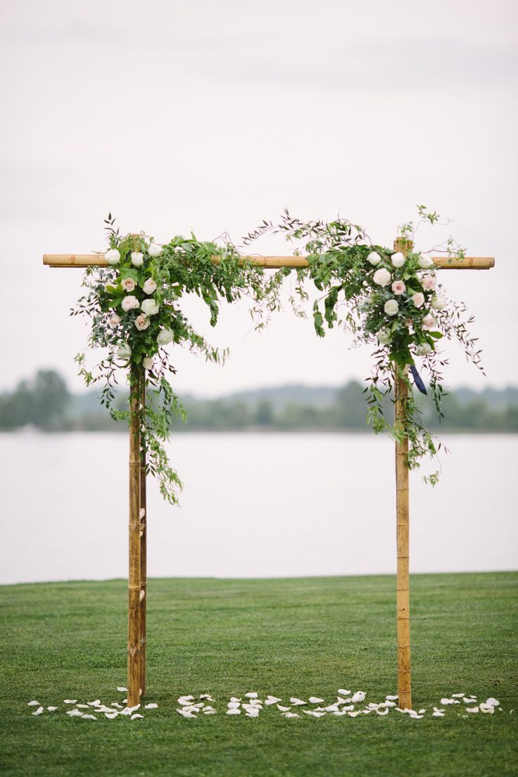 an outdoor wedding ceremony setup with flowers and greenery on the grass by the water