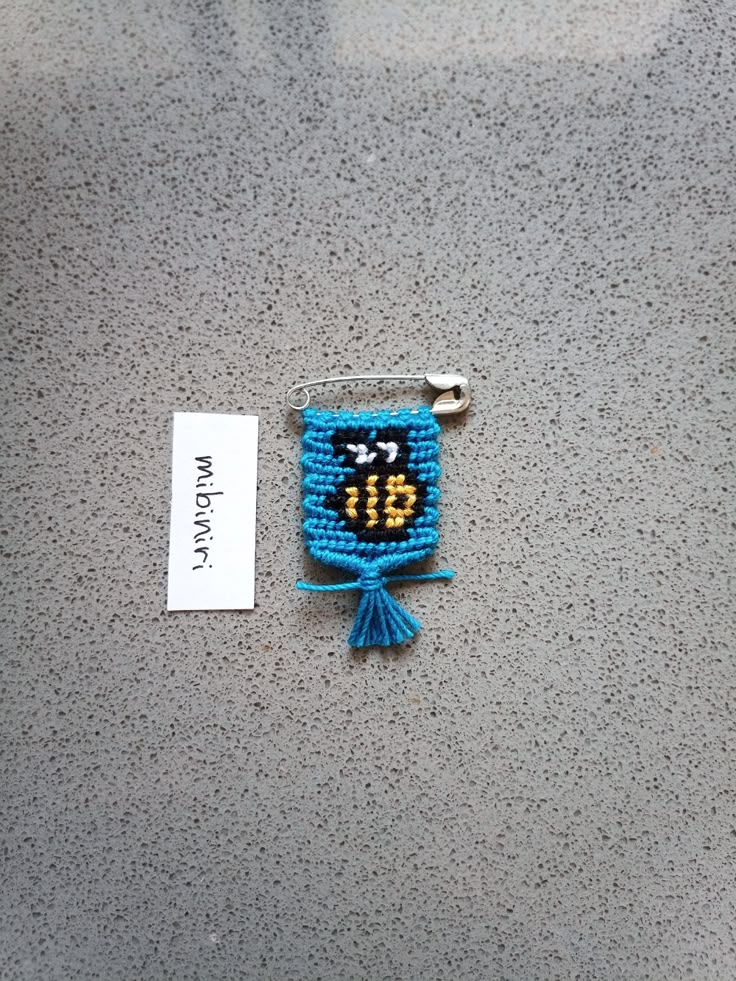 a small blue beaded object with a name tag attached to it on a gray surface