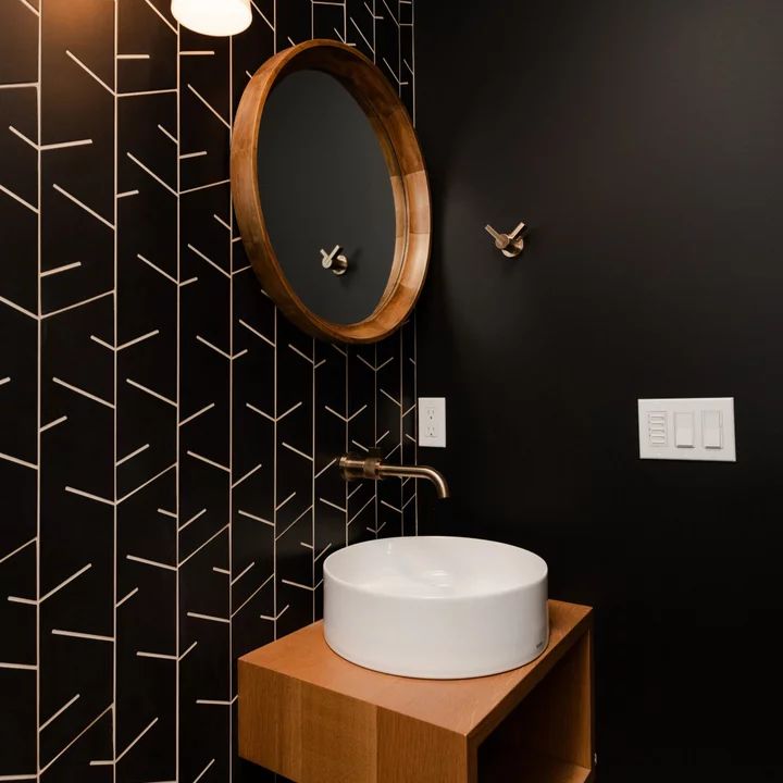 a bathroom with black and white wallpaper, round mirror and wooden sink countertop