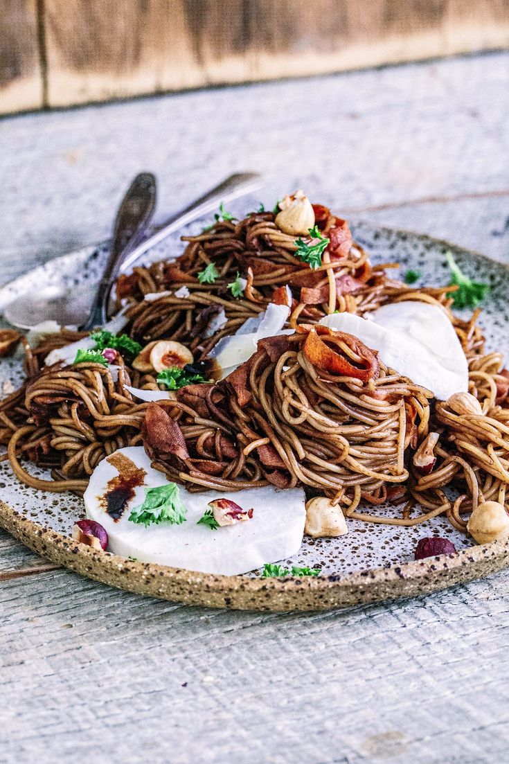 a plate filled with noodles and meat on top of a wooden table next to a fork