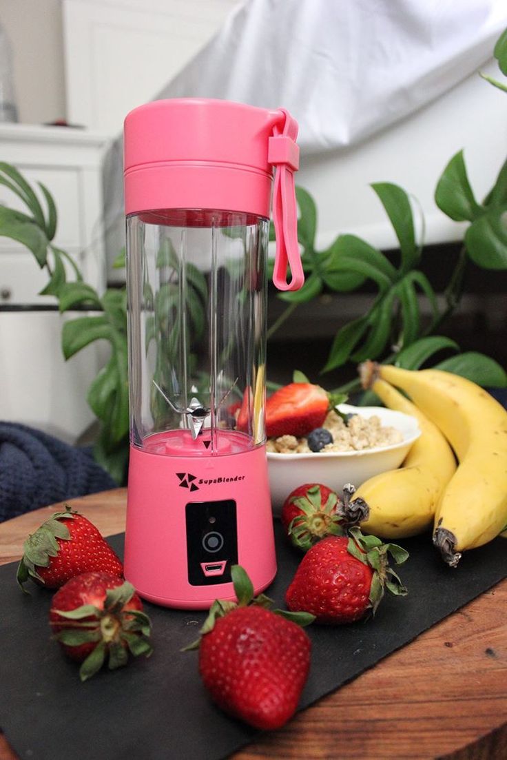 a pink blender sitting on top of a table next to bananas and strawberries