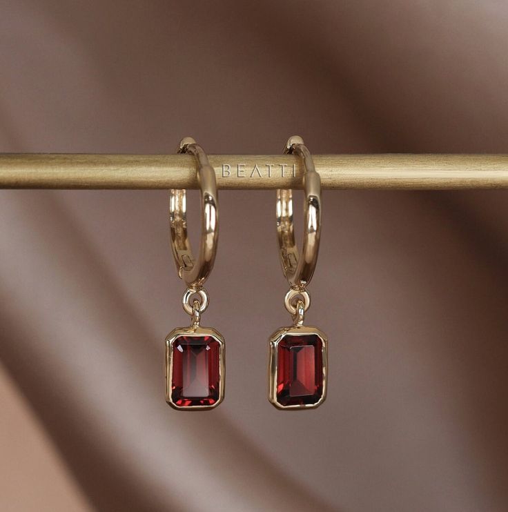 ❝ Nora: Our 14K Gold vermeil hoop earrings with a dangling charm featuring an emerald-cut garnet, beautifully framed in a bezel setting. These earrings offer a perfect blend of movement and elegance, with the rich red of the garnet providing a striking pop of color. Ideal for adding a sophisticated touch to any outfit, they're versatile for both day and night wear. ❞ ◆ PRODUCT SPECIFICATION ◆ * Material: 925 Sterling Silver - Rhodium, 14K Gold, Rose Gold * Genuine Gemstones: Garnet (4mm x 6mm) * Garnet Earrings Drop, Elegant Gold Garnet Earrings, Faceted Garnet Earrings In Gold, Garnet Faceted Earrings For Gift, Gold Faceted Garnet Earrings, Dangle Hoop Earrings, Garnet Jewelry, Night Wear, Garnet Earrings