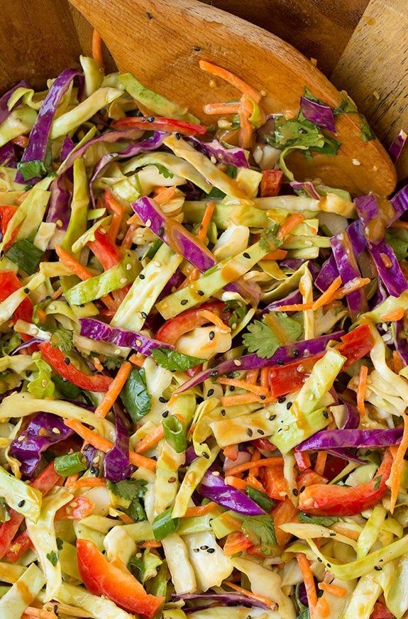 a wooden bowl filled with salad and vegetables next to a wooden spoon on top of a table