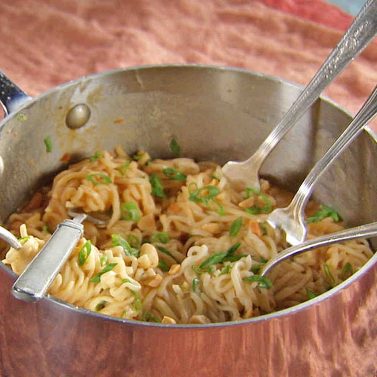 a pot full of noodles with two spoons in it on a tableclothed surface