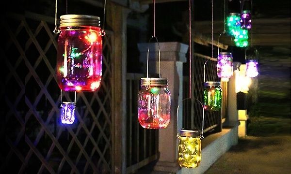 four mason jar lights hanging from the side of a building at night with colorful lights on them