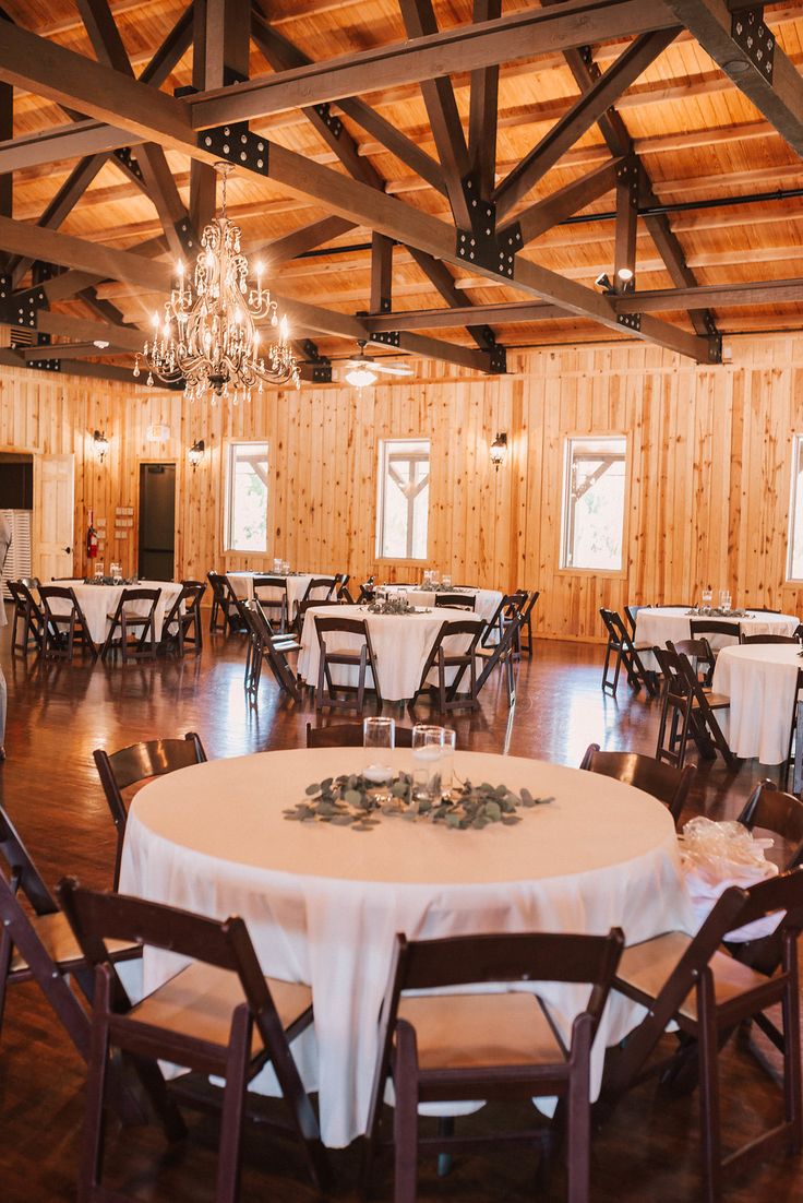 an empty banquet room with white tablecloths and wooden walls, chandeliers and windows