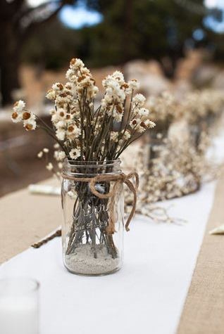 a mason jar filled with dried flowers on top of a white table cloth covered table