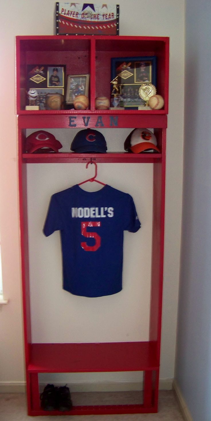 a baseball uniform and hat are on display in the corner of a room with a red shelf