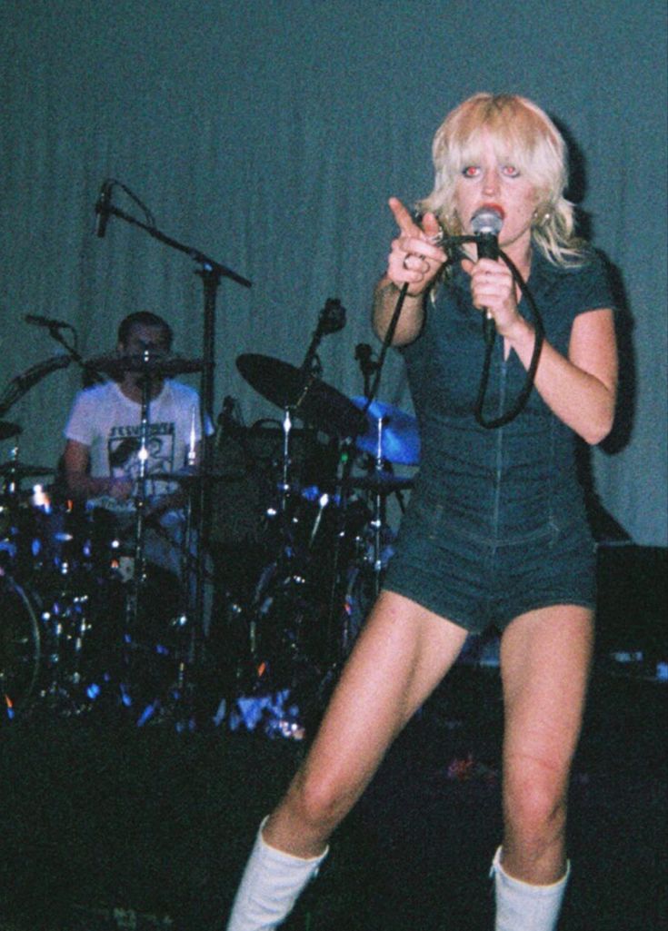 a woman standing in front of a microphone on top of a stage with other musicians behind her