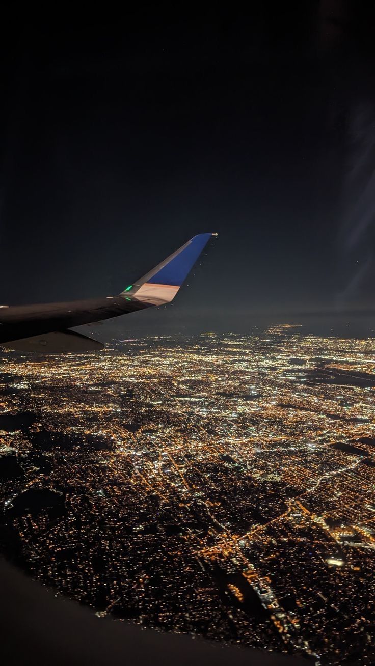 an airplane wing flying over a large city at night with lights on the buildings below