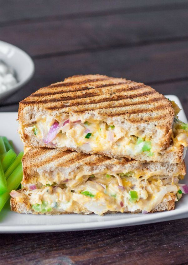 a grilled chicken salad sandwich is on a white plate next to a cup of coffee