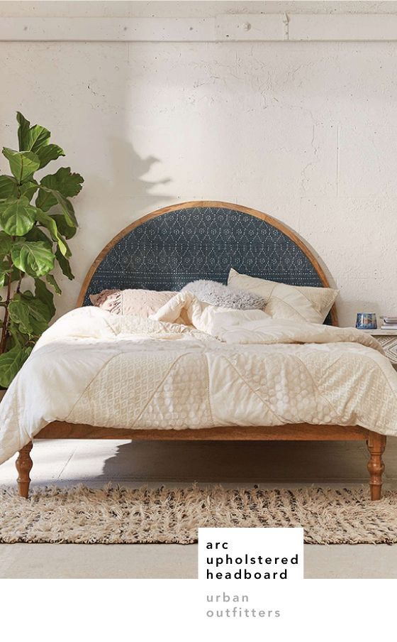 a bed with white sheets and pillows in a room next to a potted plant